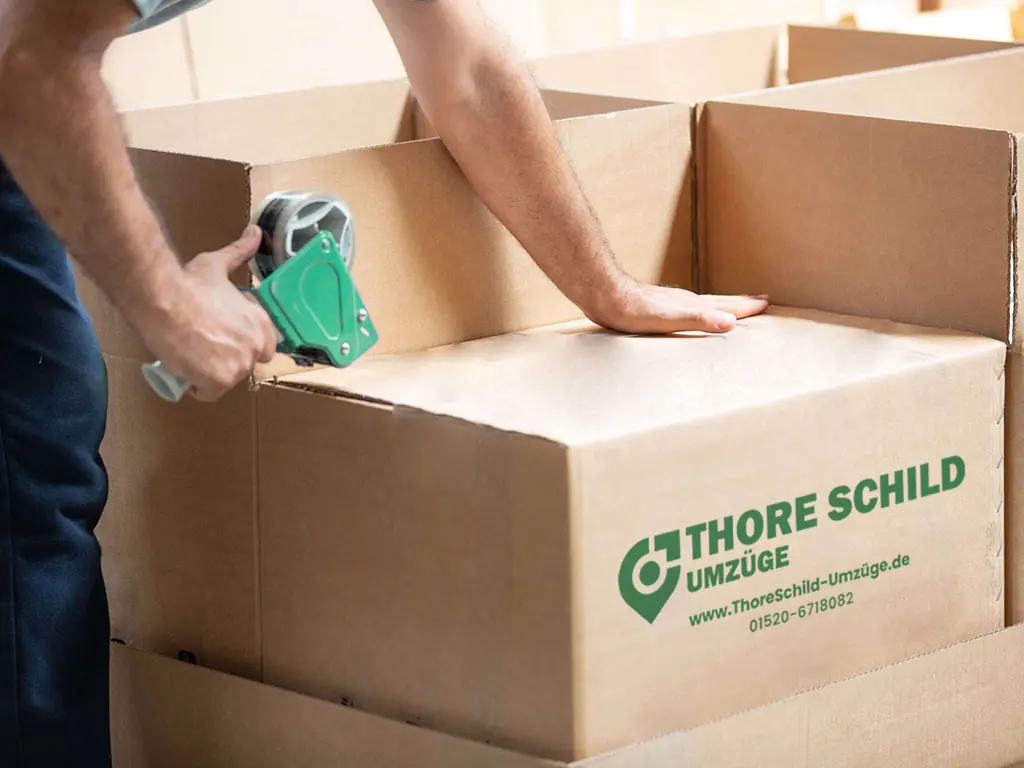 Ein Mitarbeiter von Thore Schild Umzug verschliesst einen Umzugskarton mit einem Paketband.