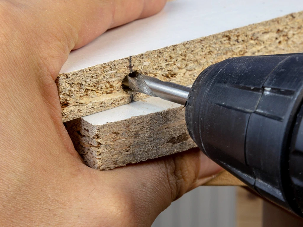 Eine Bohrmaschine bohrt ein Loch in ein Regalbrett.