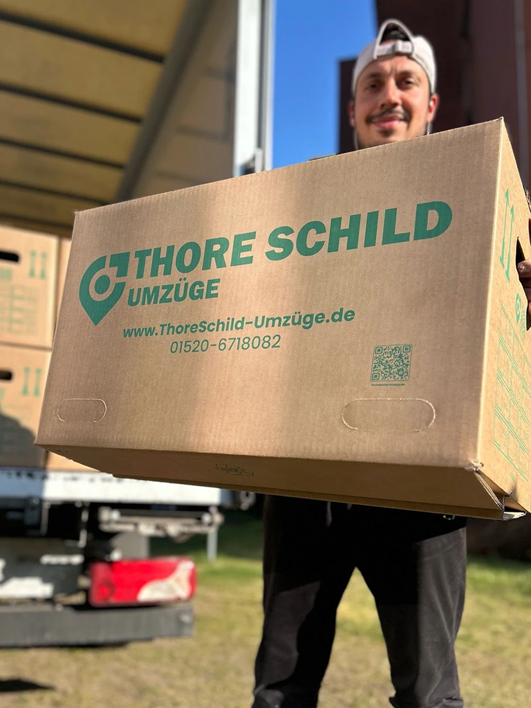 Umzugshelfer von Thore Schild Umzüge trägt einen Umzugskarton.